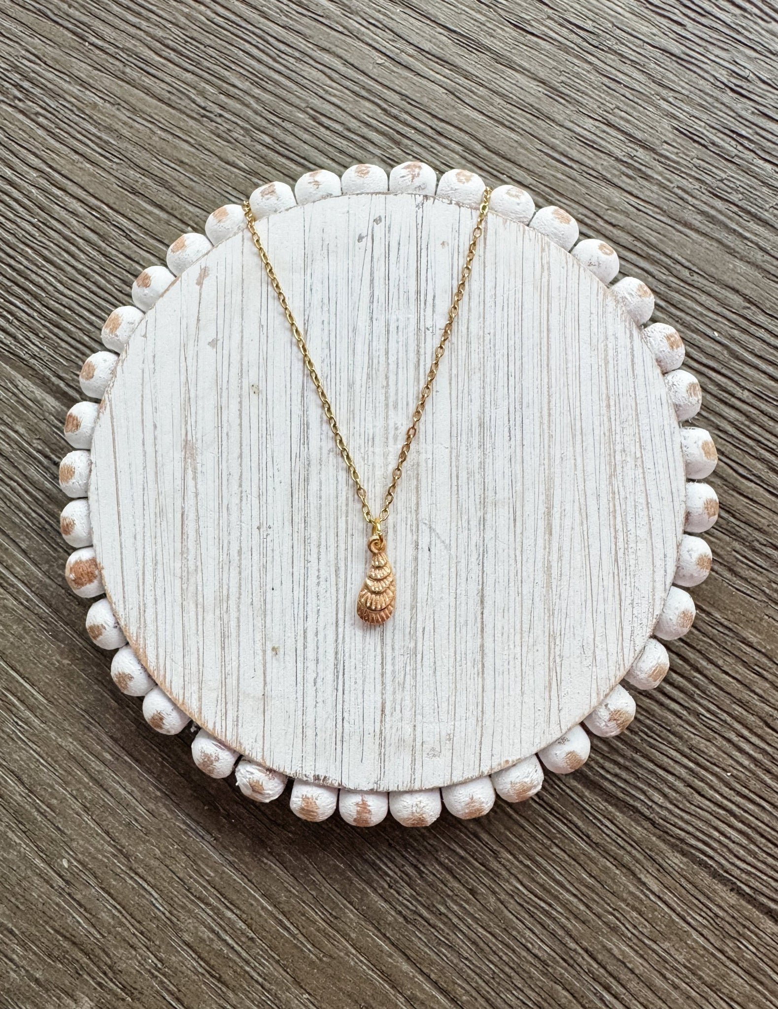 Gold necklace on a round, beaded white jewelry dish with a wooden background