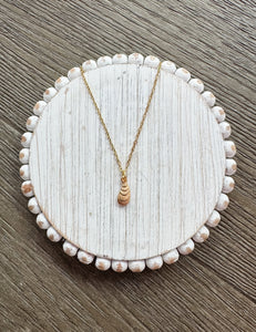Gold necklace on a round, beaded white jewelry dish with a wooden background