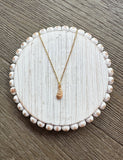 Gold necklace on a round, beaded white jewelry dish with a wooden background