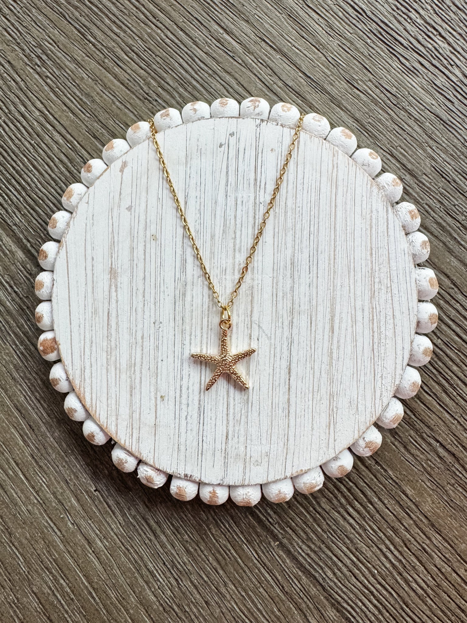 Starfish pendant necklace on a white circular stand with a wooden background
