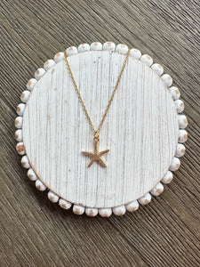 Starfish pendant necklace on a white circular stand with a wooden background