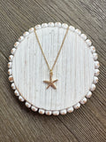 Starfish pendant necklace on a white circular stand with a wooden background